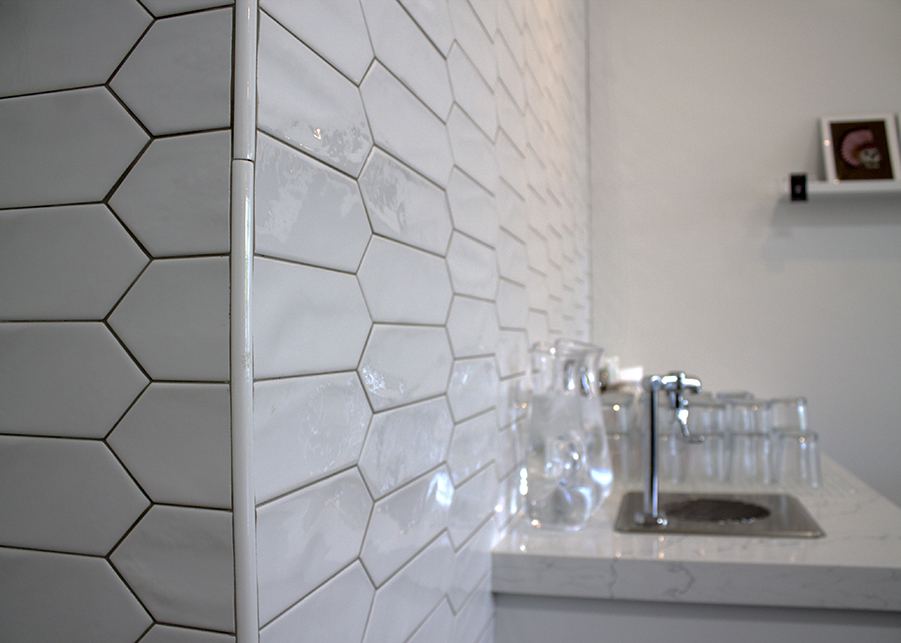A closeup of the white hexagonal subway tiles that serve as an accent wall behind the marble water station. 